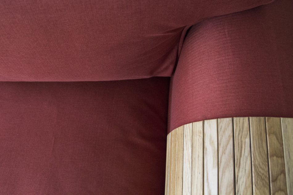 Close-up of rust-red woollen slipcovers made by Comfort Works, with a collapsible wooden sofa armrest tray in natural wood colours.