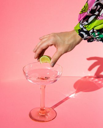 hand squeezing lime into colourless alcohol in glass