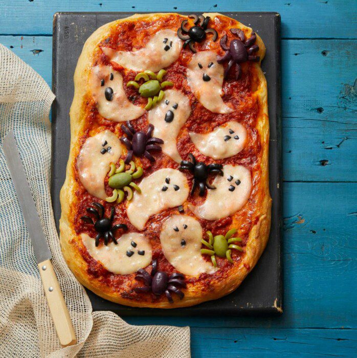 Pizza with ingredients that are arranged to look like ghosts flying around