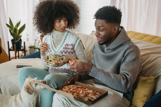 man and woman eating pizza on couch