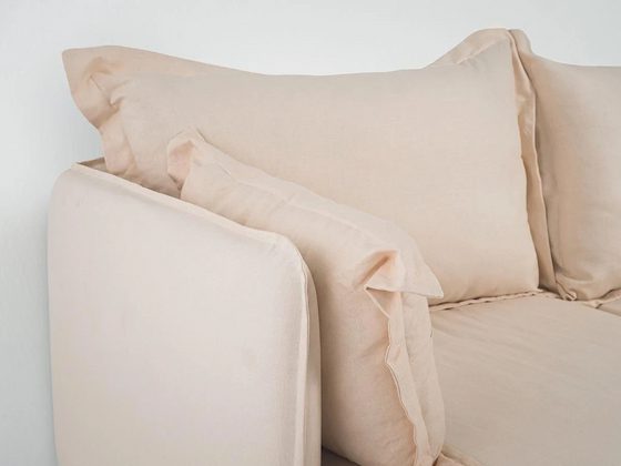 A beige sofa with extended flanges at its seams. 