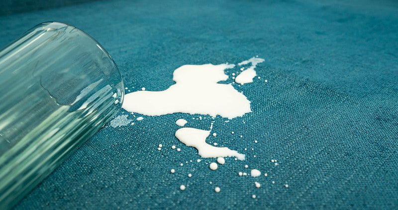 Ein verschüttetes Glas Milch auf einem blauen Sofa.