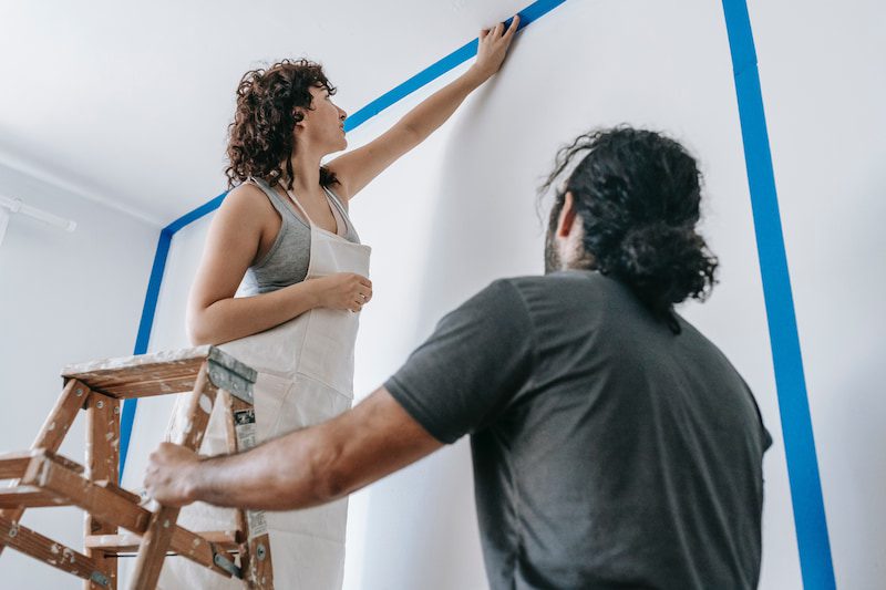 Woman and man priming wall for painting. 